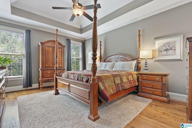 bedroom featuring crown molding, a tray ceiling, light wood-style flooring, and baseboards