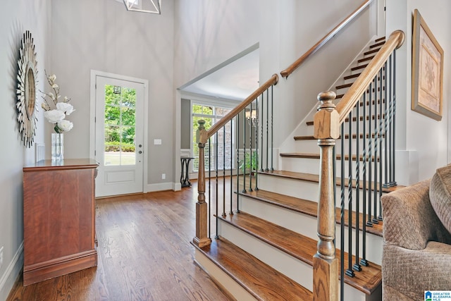 foyer entrance with stairway, a towering ceiling, baseboards, and wood finished floors