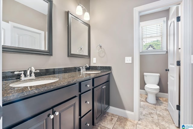 bathroom featuring toilet, a sink, baseboards, and double vanity