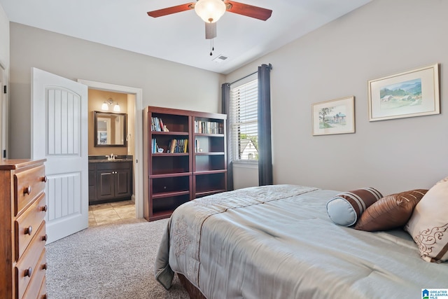 bedroom featuring light colored carpet, visible vents, a ceiling fan, a sink, and ensuite bath