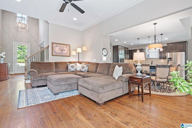 living area featuring recessed lighting, stairway, light wood-style floors, ornamental molding, and ceiling fan with notable chandelier