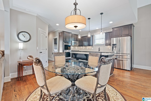 dining space with ornamental molding, recessed lighting, baseboards, and light wood finished floors