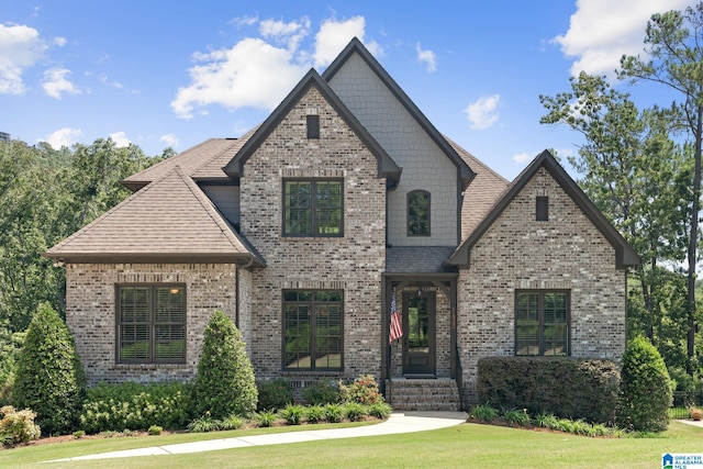 view of front of house featuring brick siding, a front yard, and a shingled roof