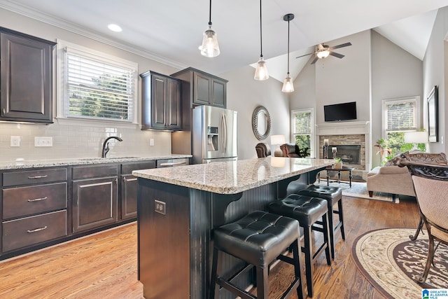 kitchen with stainless steel fridge with ice dispenser, open floor plan, a sink, dark brown cabinetry, and a kitchen breakfast bar