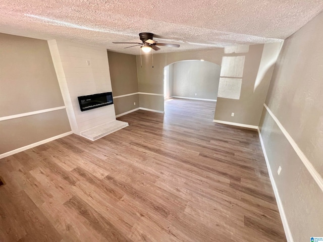 unfurnished living room with a fireplace, ceiling fan, hardwood / wood-style floors, and a textured ceiling