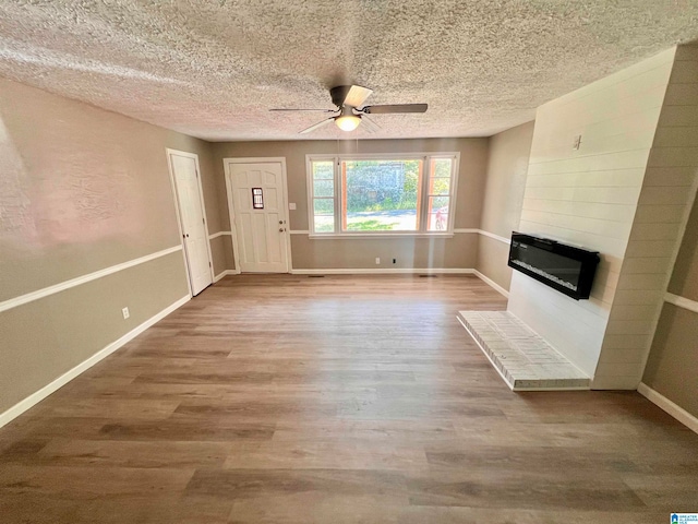 unfurnished living room featuring ceiling fan, a large fireplace, hardwood / wood-style flooring, and a textured ceiling