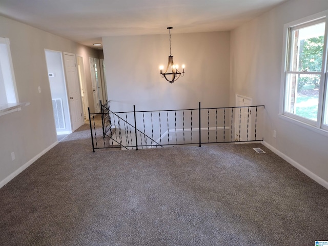 carpeted empty room featuring a healthy amount of sunlight and an inviting chandelier