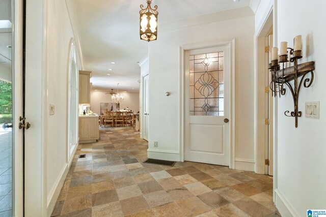 doorway to outside with crown molding, light tile patterned flooring, and an inviting chandelier