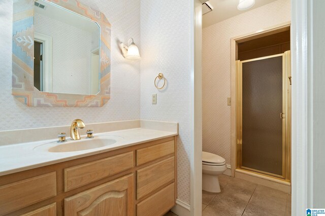 bathroom with a shower with shower door, toilet, vanity, and tile patterned floors