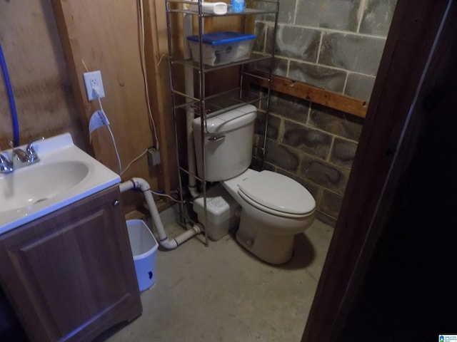 half bathroom with concrete block wall, vanity, and toilet