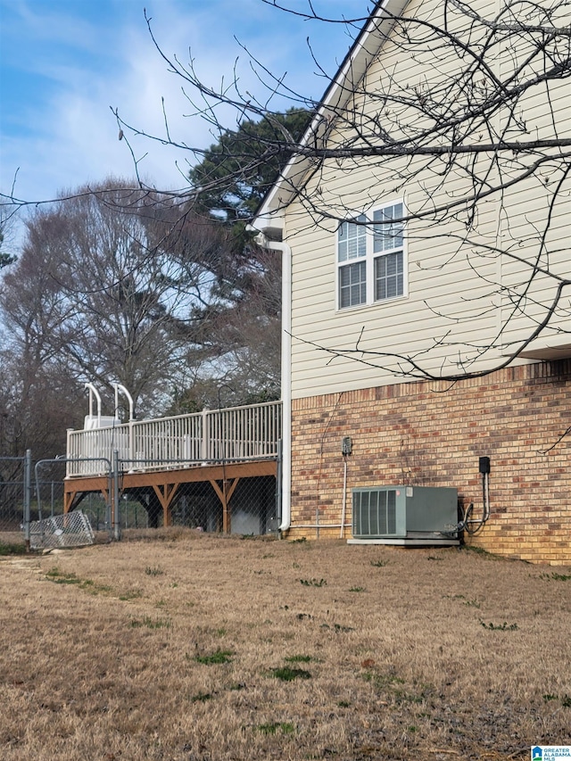 view of side of home featuring a deck, a yard, brick siding, and cooling unit