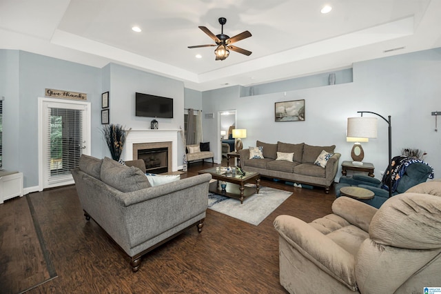 living room with a raised ceiling, ceiling fan, and dark hardwood / wood-style floors