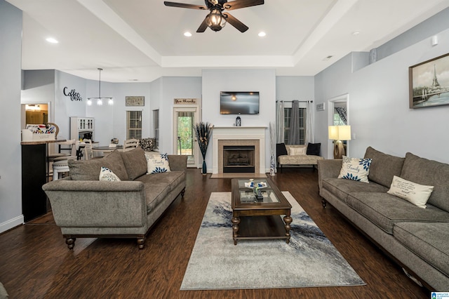 living room featuring a tray ceiling, dark wood-type flooring, ceiling fan, and a tile fireplace