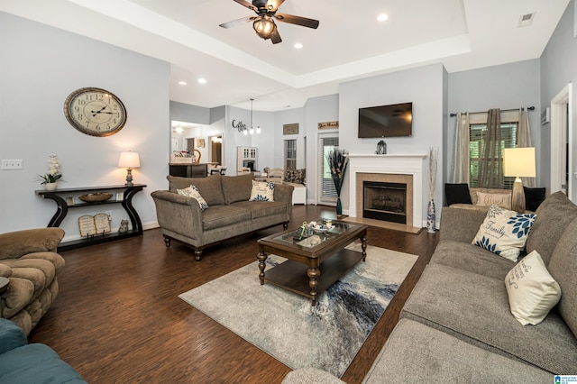 living room with dark wood-type flooring, ceiling fan with notable chandelier, and a raised ceiling