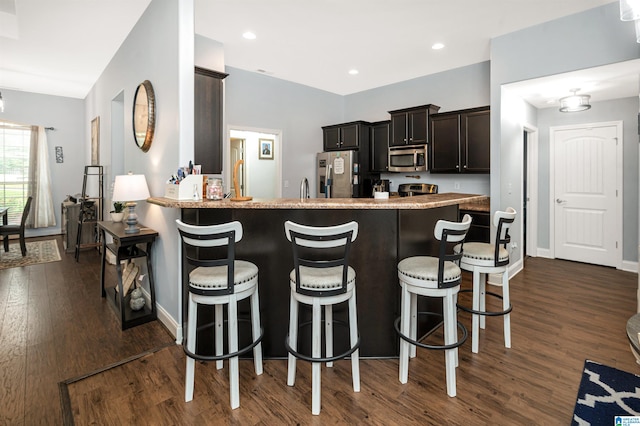 kitchen featuring stainless steel appliances, dark hardwood / wood-style floors, kitchen peninsula, and a breakfast bar area