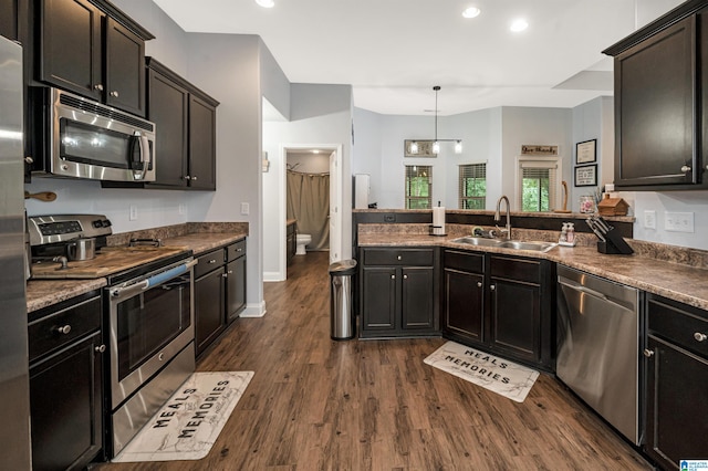 kitchen featuring pendant lighting, stainless steel appliances, kitchen peninsula, sink, and dark hardwood / wood-style floors