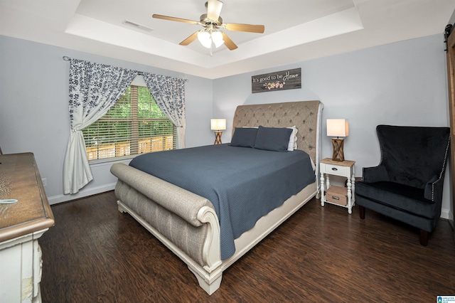 bedroom with a tray ceiling, dark hardwood / wood-style floors, and ceiling fan