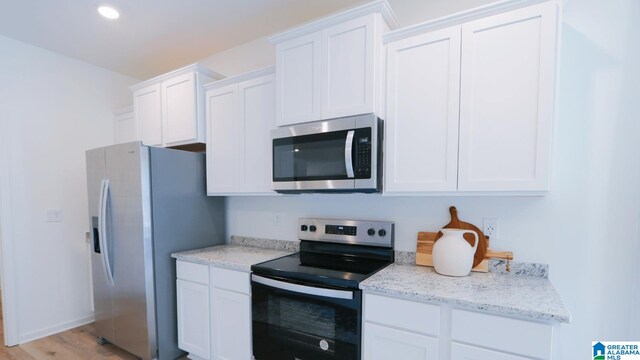 kitchen featuring stainless steel appliances, white cabinets, light hardwood / wood-style flooring, and light stone counters