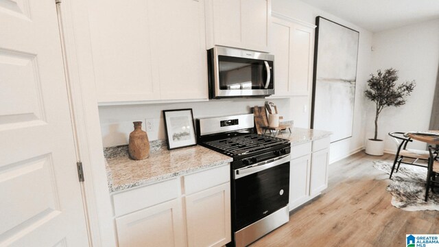 kitchen featuring white cabinets, appliances with stainless steel finishes, light hardwood / wood-style floors, and light stone counters