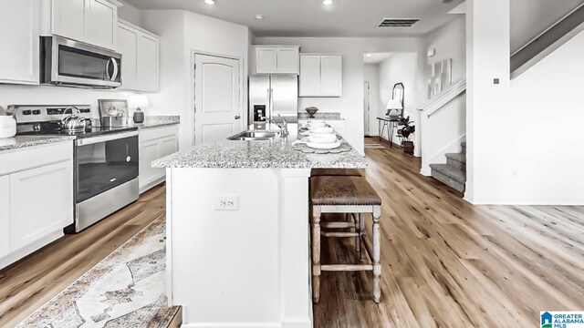 kitchen with white cabinets, light hardwood / wood-style floors, a kitchen island with sink, and appliances with stainless steel finishes