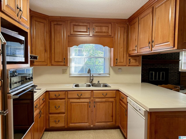 kitchen with wall oven, a sink, light countertops, brown cabinets, and dishwasher