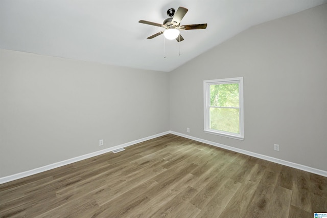 empty room with lofted ceiling, wood finished floors, a ceiling fan, and baseboards