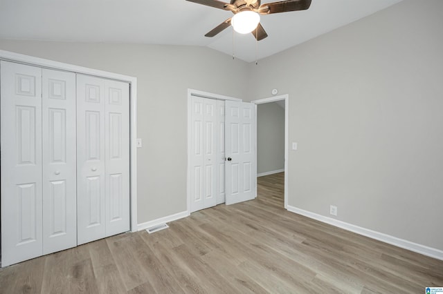 unfurnished bedroom featuring two closets, visible vents, vaulted ceiling, wood finished floors, and baseboards