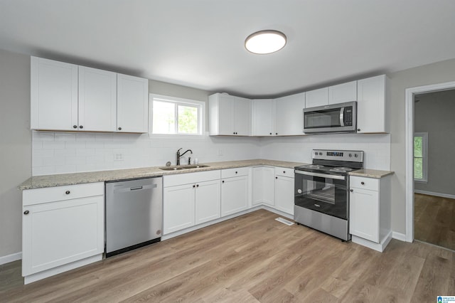 kitchen featuring appliances with stainless steel finishes, light wood-type flooring, a sink, and white cabinetry