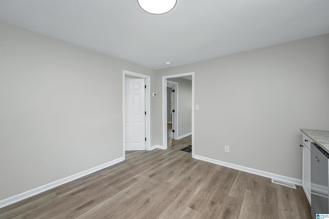 spare room featuring light wood finished floors, visible vents, and baseboards