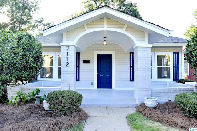 property entrance with brick siding, a porch, and a shingled roof