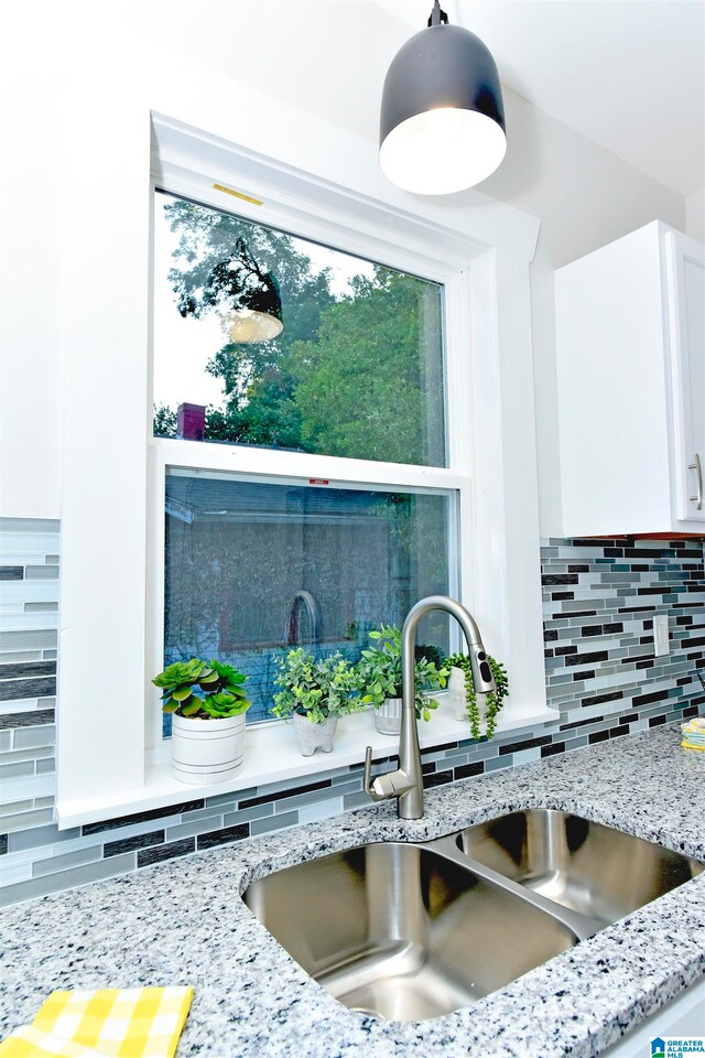 interior details featuring tasteful backsplash, white cabinets, light stone counters, sink, and decorative light fixtures