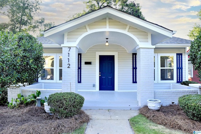 view of exterior entry with brick siding, a porch, and a shingled roof