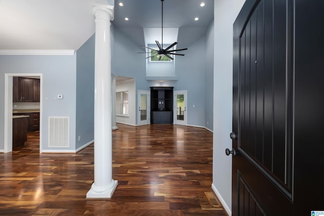 foyer entrance with crown molding, a towering ceiling, dark hardwood / wood-style flooring, and ornate columns