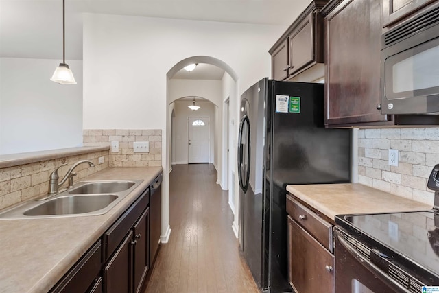 kitchen with pendant lighting, hardwood / wood-style floors, black appliances, sink, and decorative backsplash