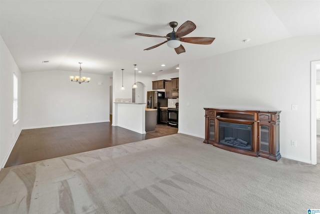 unfurnished living room featuring lofted ceiling, ceiling fan with notable chandelier, and carpet floors