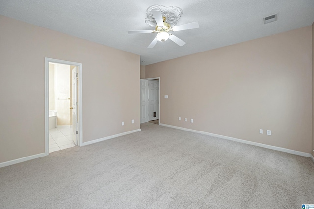 unfurnished bedroom with ceiling fan, a textured ceiling, light carpet, and ensuite bath