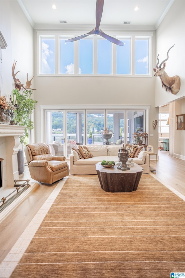 living room with light wood-style floors, plenty of natural light, a fireplace with raised hearth, and crown molding