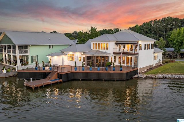 back of property at dusk featuring metal roof, a water view, and a balcony