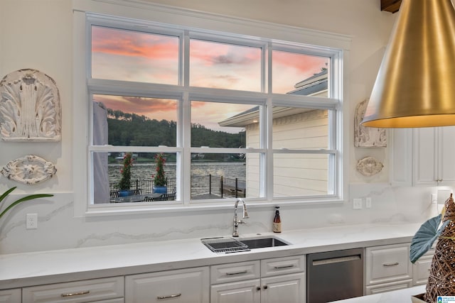 kitchen with a wealth of natural light, a water view, white cabinets, a sink, and dishwasher