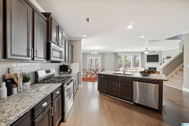 kitchen featuring backsplash, dark brown cabinets, ornamental molding, stainless steel appliances, and a sink