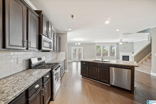 kitchen with a sink, appliances with stainless steel finishes, open floor plan, and ornamental molding