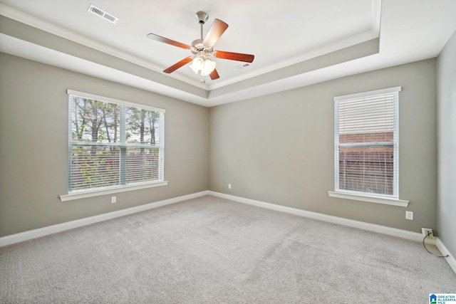 carpeted empty room with baseboards, visible vents, a tray ceiling, ornamental molding, and ceiling fan