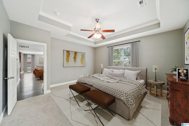 bedroom with a tray ceiling, baseboards, visible vents, and light carpet