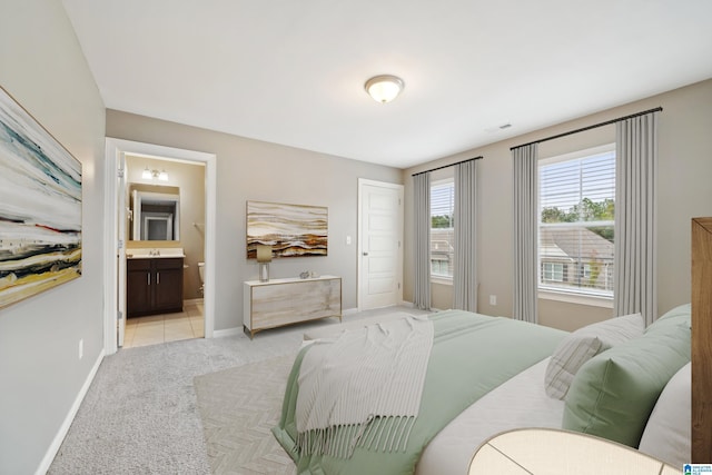 bedroom featuring a sink, ensuite bath, a closet, baseboards, and light colored carpet