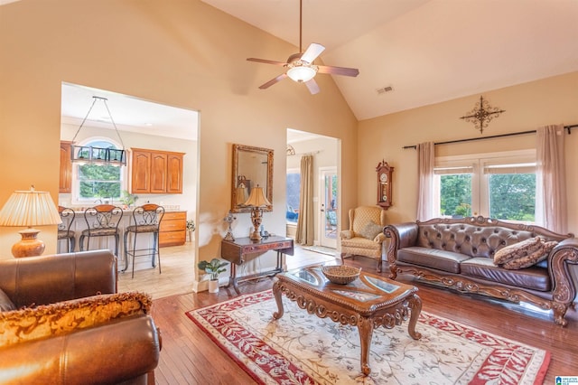 living area with ceiling fan, high vaulted ceiling, light wood-type flooring, and visible vents