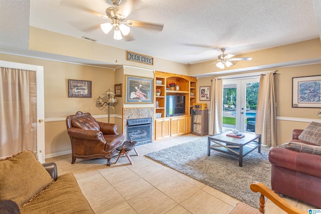 living room featuring a textured ceiling, built in shelves, a fireplace, visible vents, and french doors