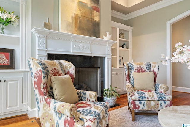 living room featuring baseboards, wood finished floors, ornamental molding, and a tile fireplace