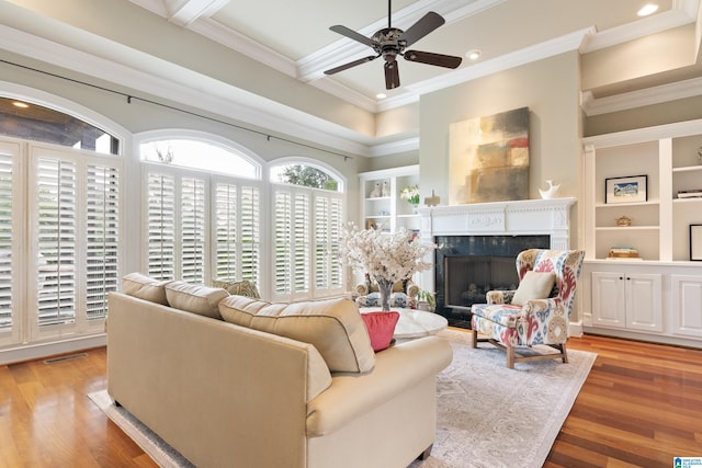 living room with a high end fireplace, crown molding, beamed ceiling, wood finished floors, and a ceiling fan