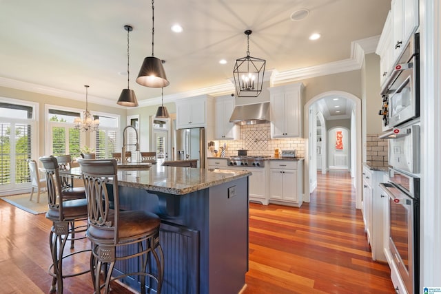 kitchen featuring a chandelier, a breakfast bar, stainless steel appliances, wall chimney exhaust hood, and a sink