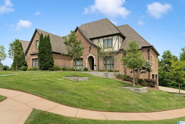 tudor home featuring a front yard, brick siding, and roof with shingles